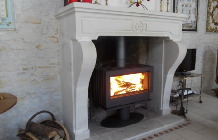 Insert à bois moderne installé dans un ancien foyer ouvert, avec flamme visible et cheminée en pierre rénovée.