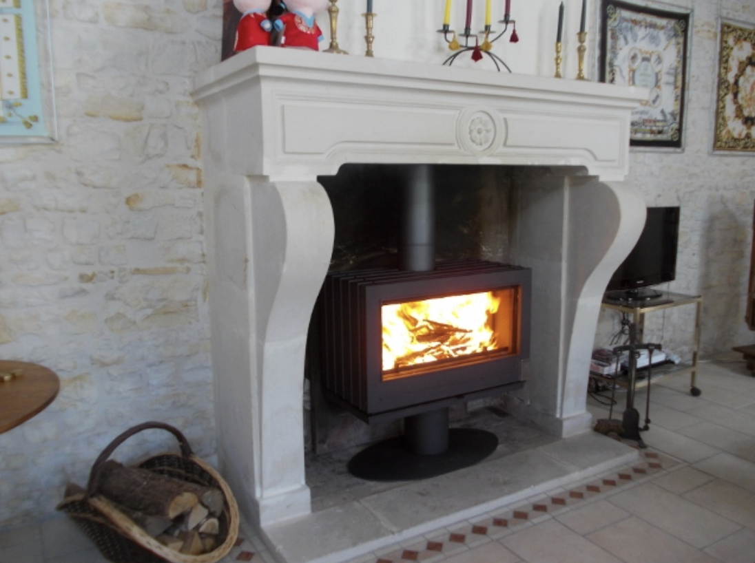 Insert à bois moderne installé dans un ancien foyer ouvert, avec flamme visible et cheminée en pierre rénovée.